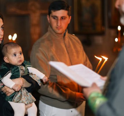 A family participates in a traditional religious ceremony with candlelight indoors.