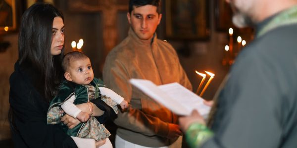 A family participates in a traditional religious ceremony with candlelight indoors.